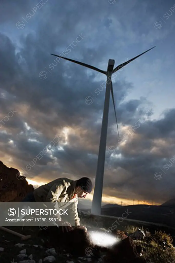 Man Burying Light Bulb with Wind Turbine in Background   
