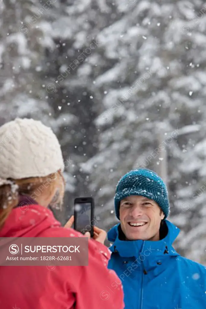 Woman Taking Picture of Man with Camera Phone Outdoors in Winter, Whistler, British Columbia, Canada