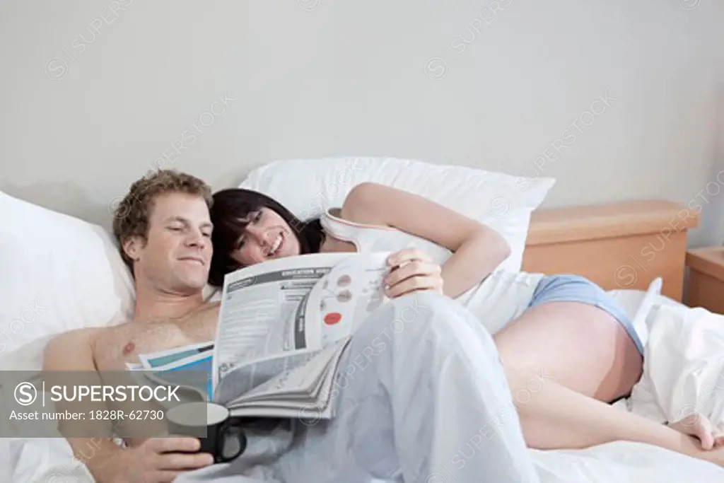 Couple Relaxing in Bed With Coffee and the Newspaper