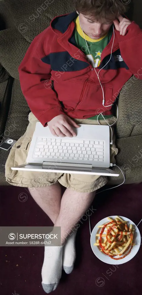 Student Sitting on Couch With Laptop Computer and Plate of French Fries