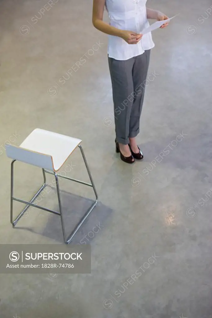 Businesswoman Standing Next to Chair, Reading Document