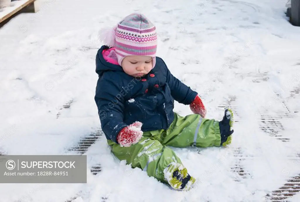 Baby Girl wearing Snow Suit sitting on Ground in Snow