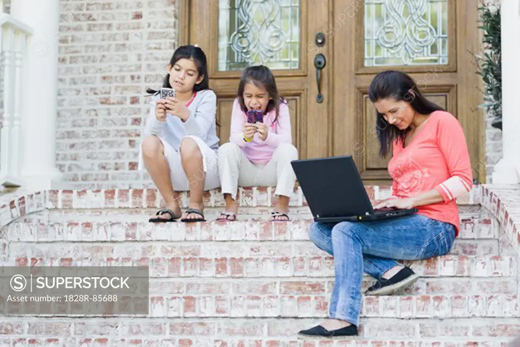 Mother using Laptop and Daughters using Handheld Video Games