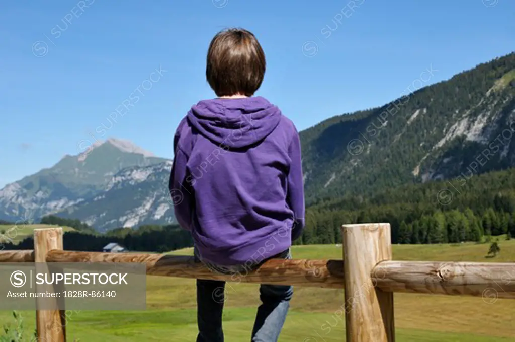 Back View of Boy Sitting on Wooden Fence, Glieres Plateau, Alps, France