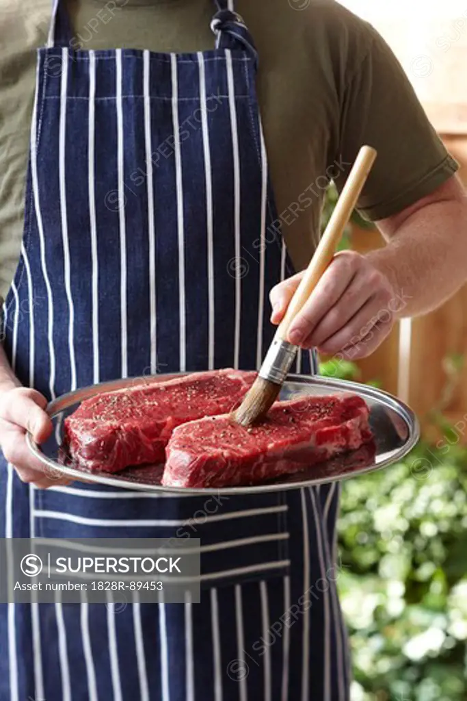 Man Brushing Steaks with Olive Oil