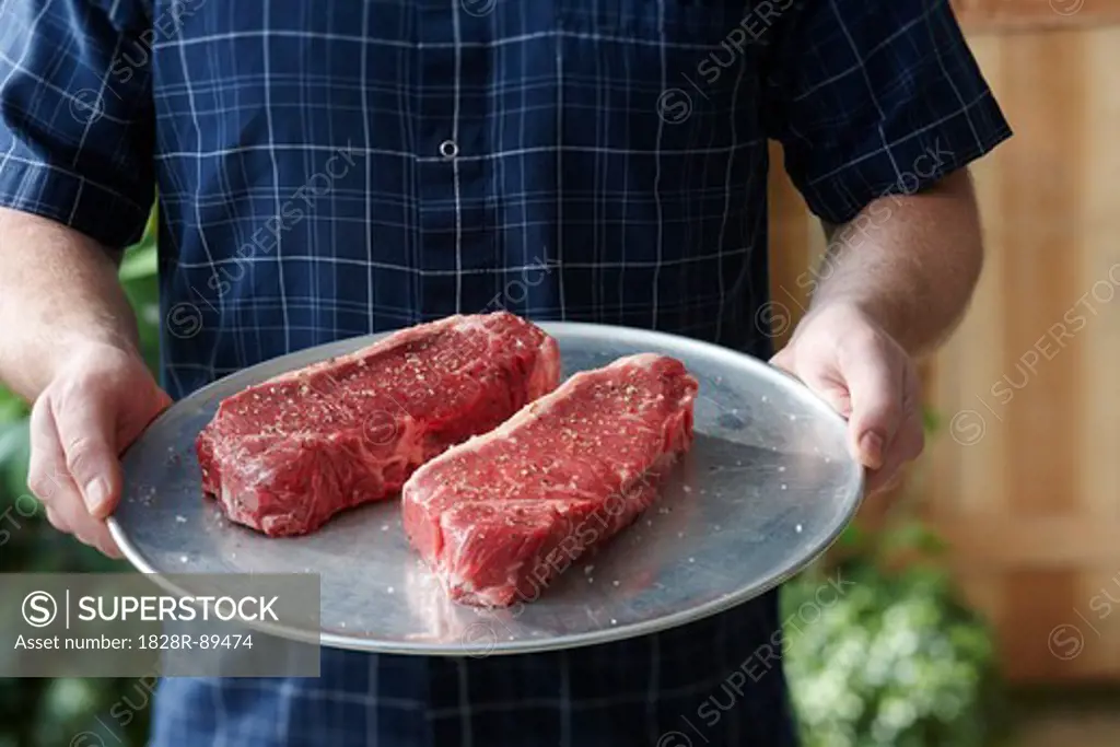 Man holding Tray with Raw Steaks
