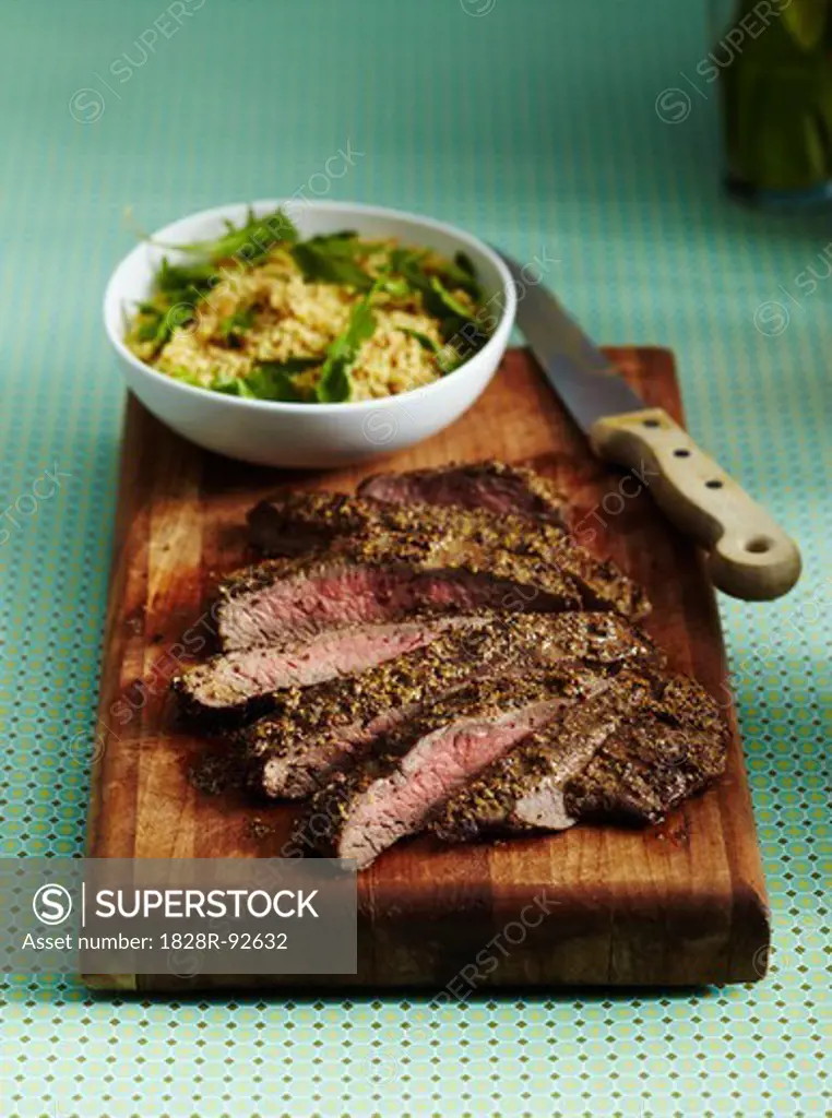 Sliced Flank Steak and Salad on Wodden Cutting Board with Knife on Turquoise Background in Studio