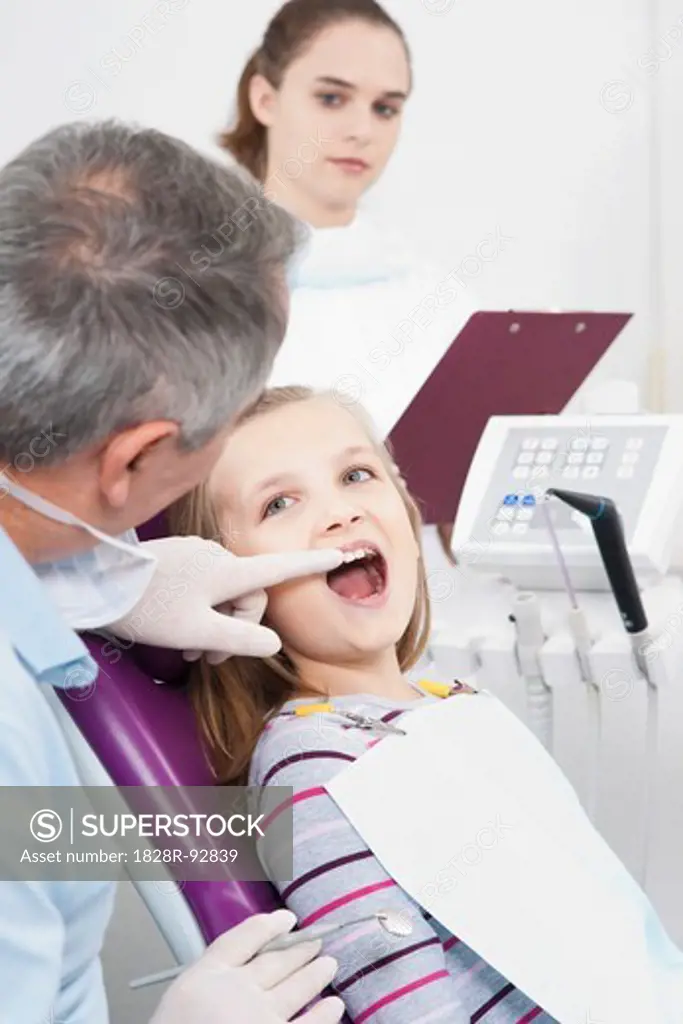 Dentist touching Girl's tooth and Hygienist with Clipboard during Appointment, Germany