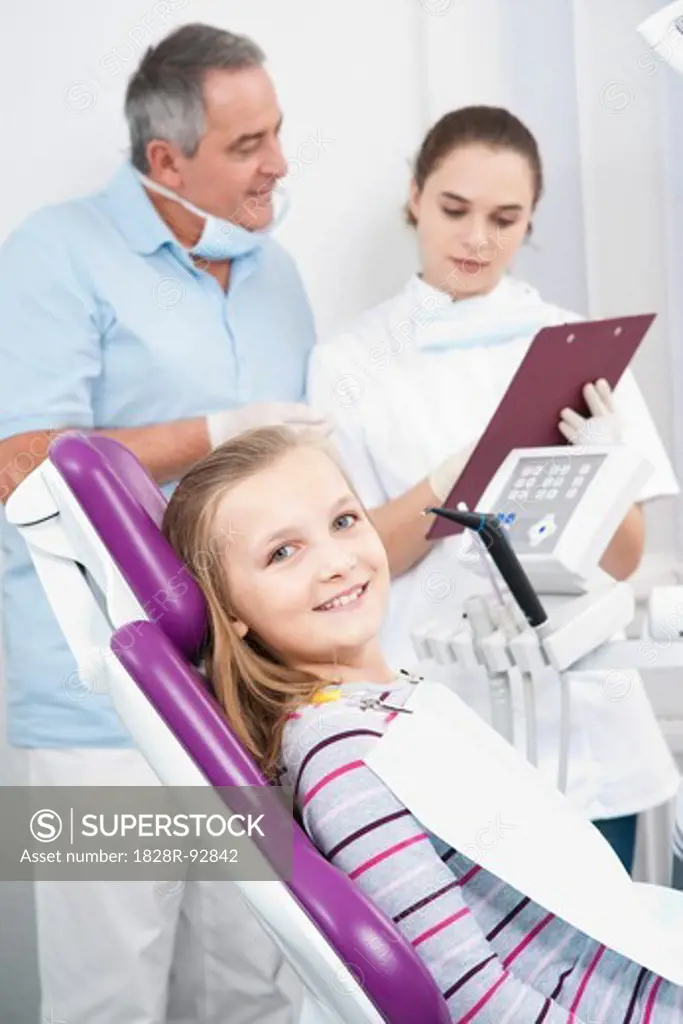 Portrait of Girl at Dentist's Office with Dentist and Hygienist in background looking at Medical Chart, Germany
