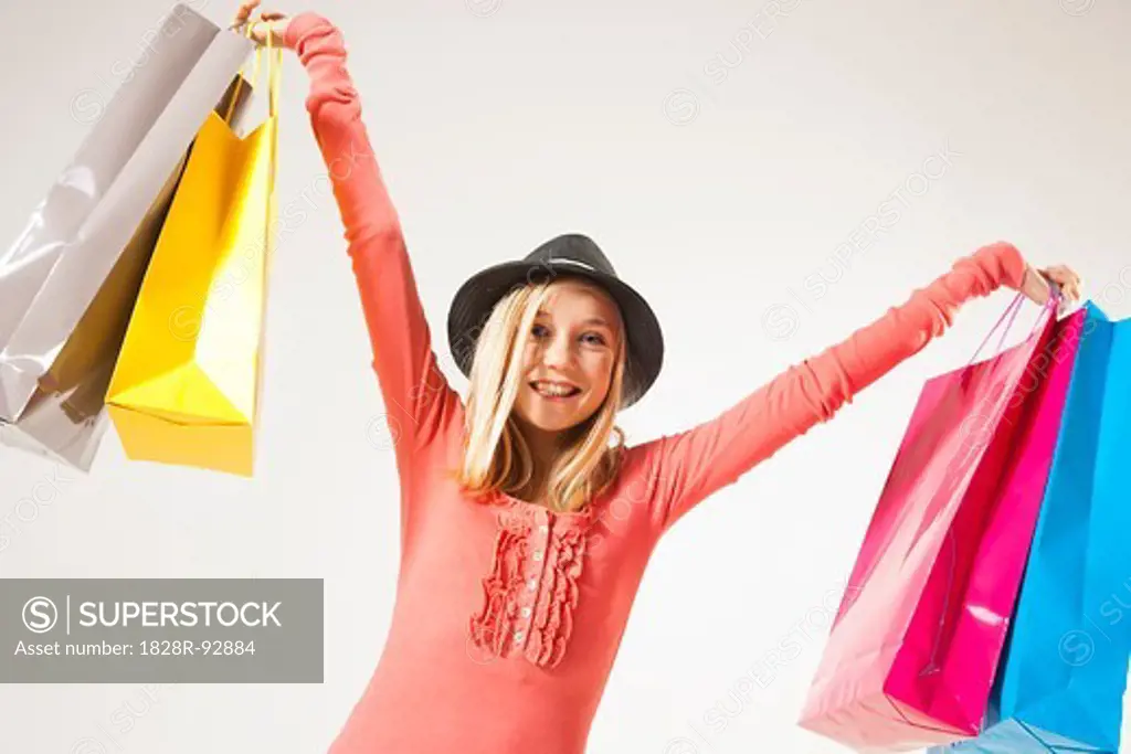 Low Angle View Portrait of Blond, Teenage Girl wearing Hat and holding Shopping Bags in Air, Studio Shot on White Background