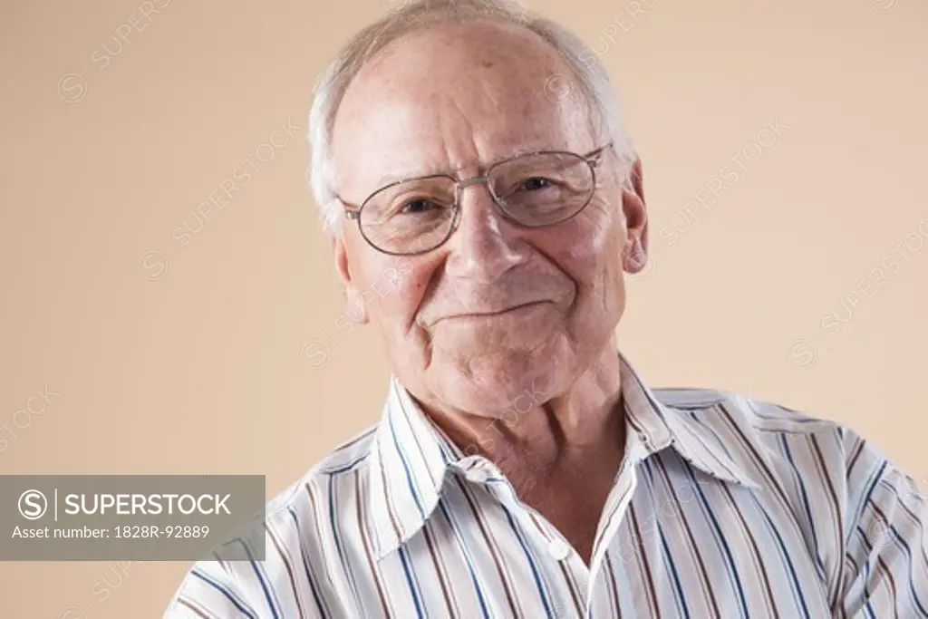 Portrait of Senior Man wearing Aviator Eyeglasses, Looking at Camera Smiling, in Studio on Beige Background