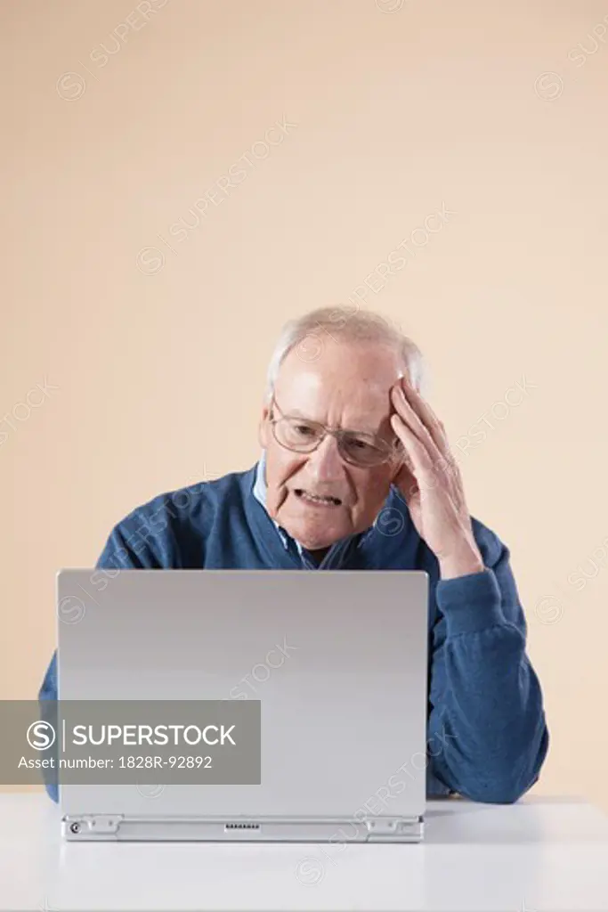 Senior Man Sitting Sitting at Table using Laptop Computer looking Confused, Studio Shot on Beige Background