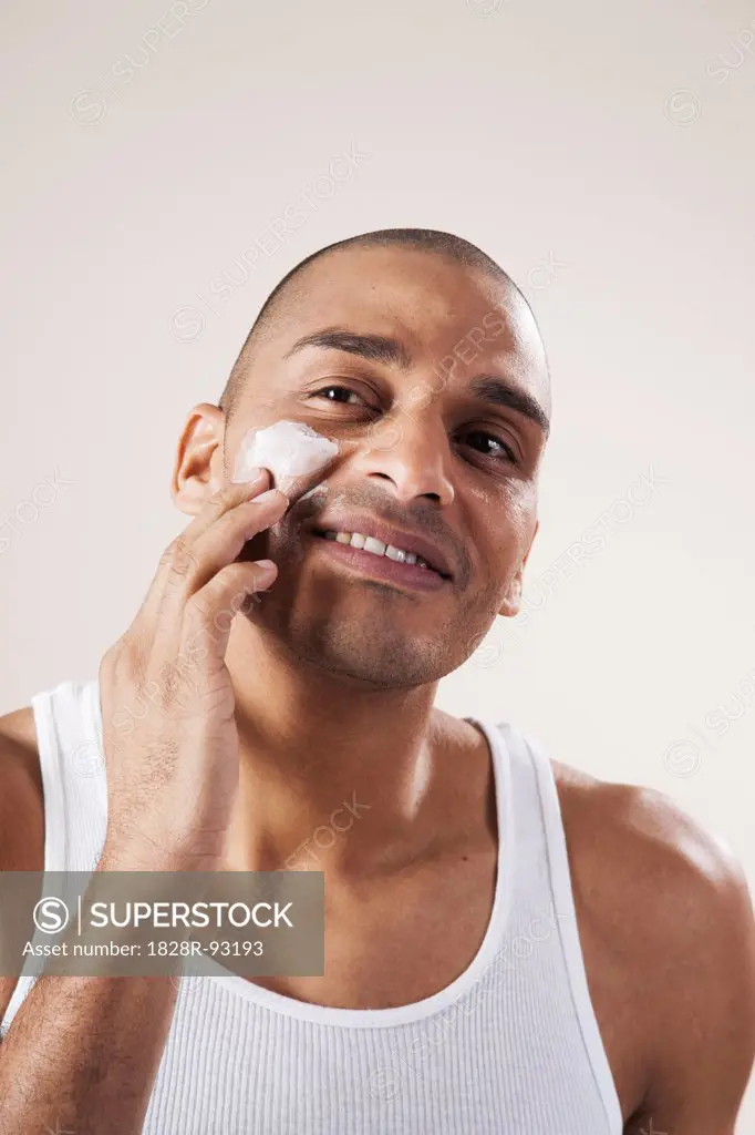 Man Applying Lotion to his Face in Studio with White Background