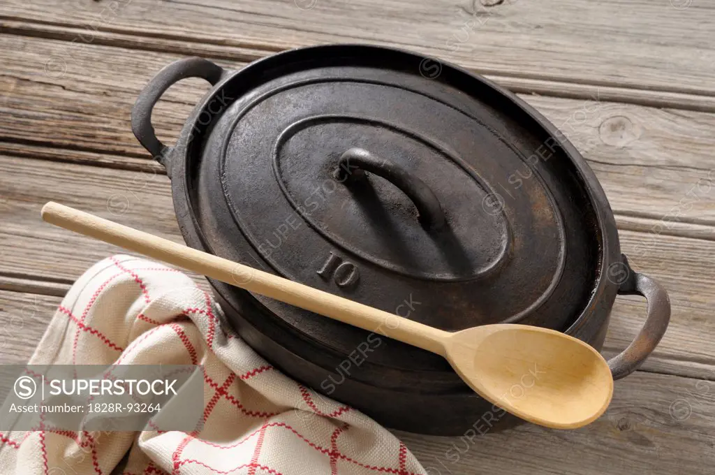 Overhead View of Cast Iron Cooking Pot with Wooden Spoon and Tea Towel on Wooden Table