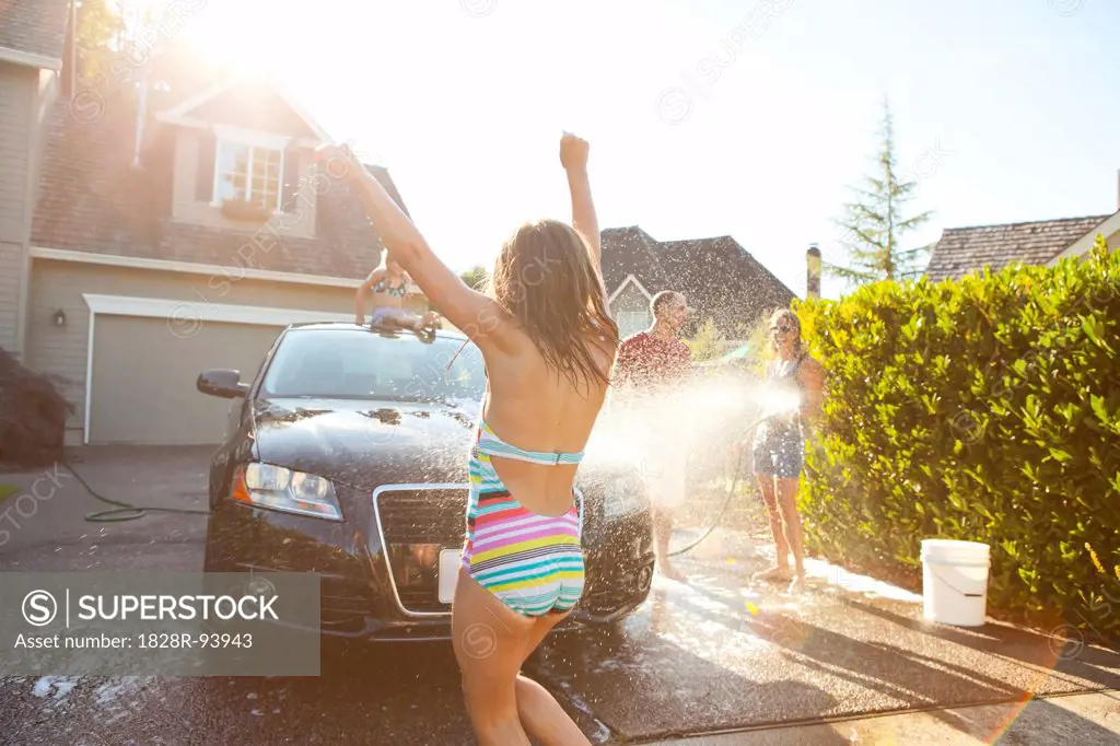 Young girl dances while family washes their car in the driveway of their home on a sunny summer afternoon in Portland, Oregon, USA