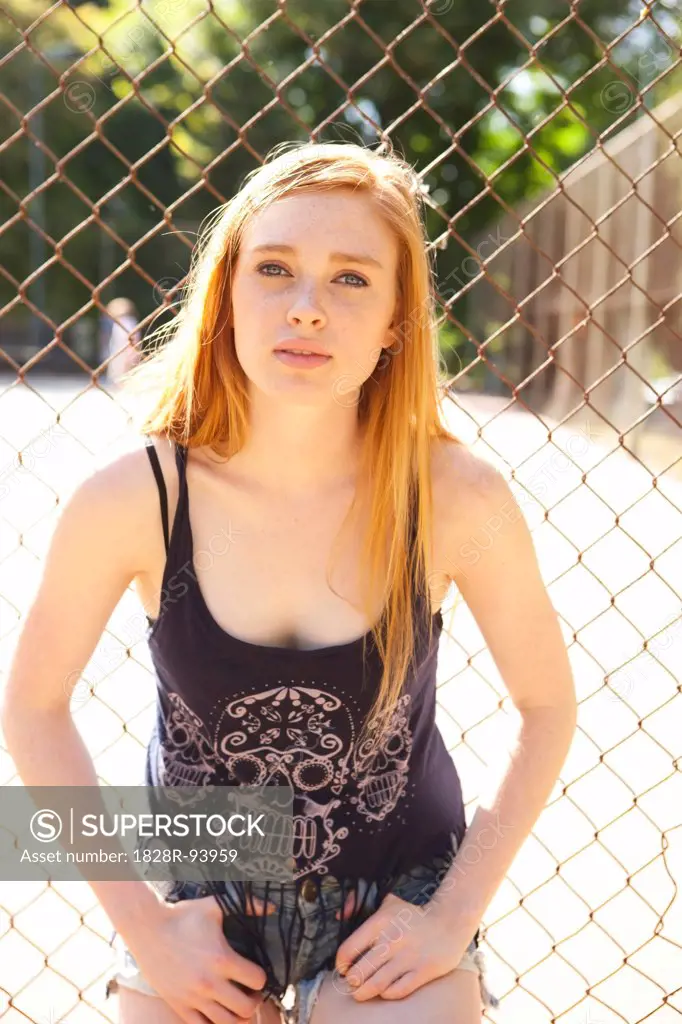 Portrait of young woman standing in front of chain link fence in park near the tennis court on a warm summer day in Portland, Oregon, USA