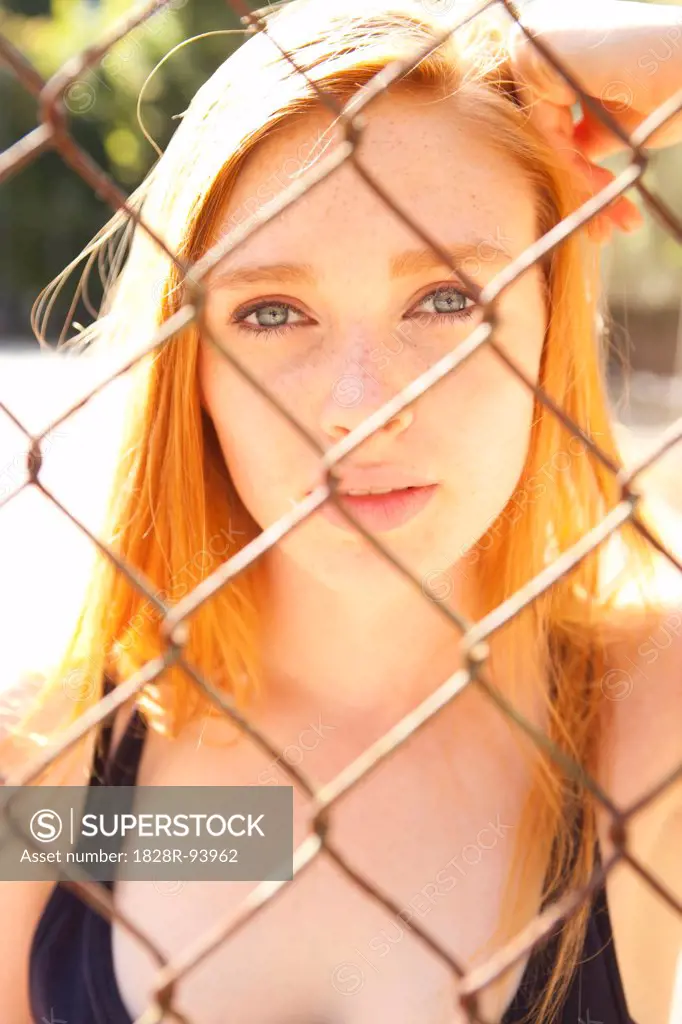 Close-up portrait of young woman standing behind chain link fence in park near the tennis court on a warm summer day in Portland, Oregon, USA