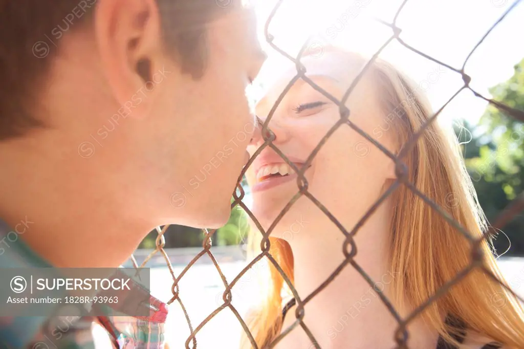 Young couple kissing through chain link fence in park near the tennis court on a warm summer day in Portland, Oregon, USA