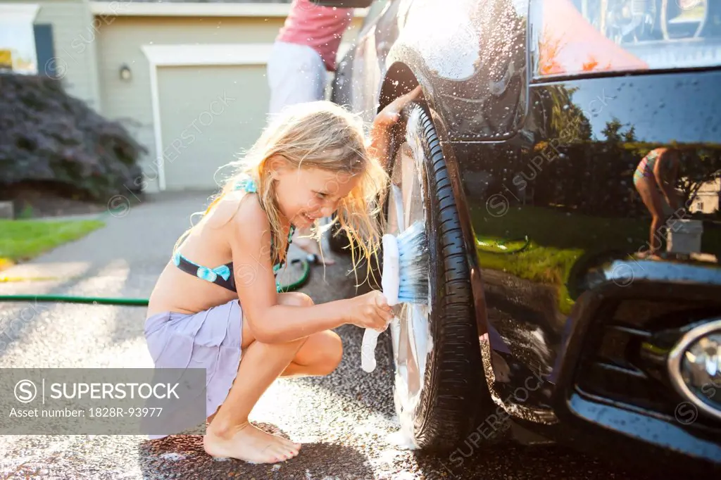 Young daughters help father wash their car in the driveway of their home on a sunny summer afternoon in Portland, Oregon, USA