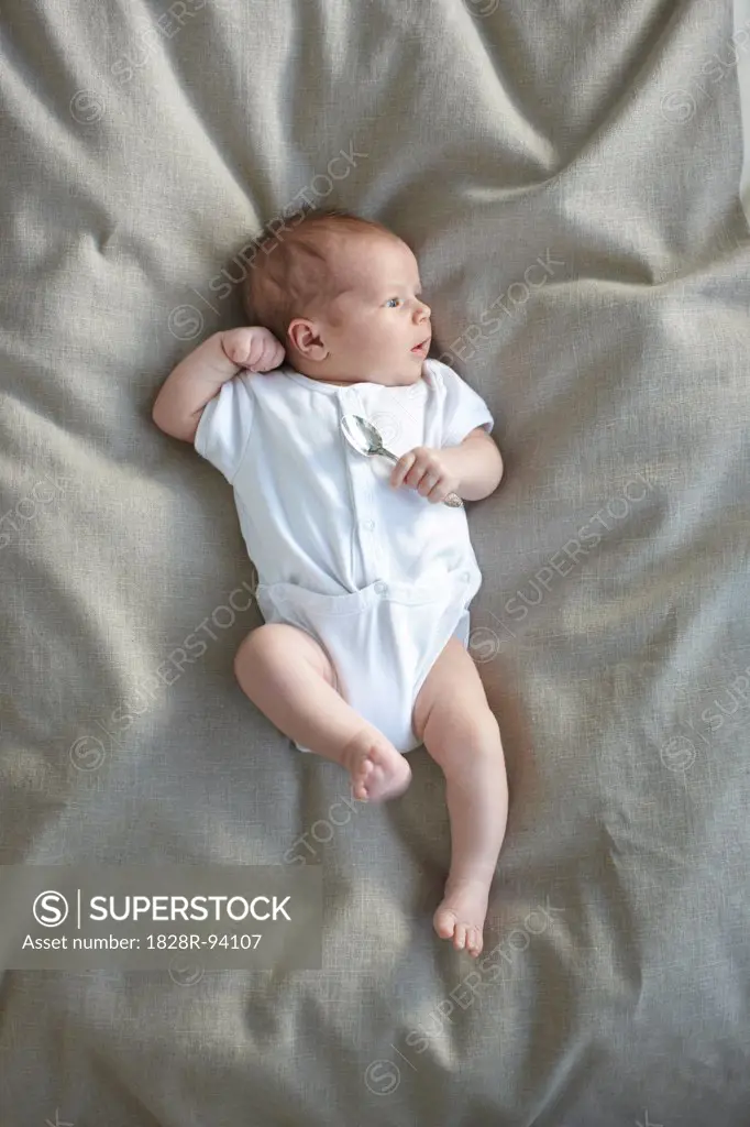 newborn baby girl in a white undershirt laying on a bed with a silver spoon in her hand, Ontario, Canada