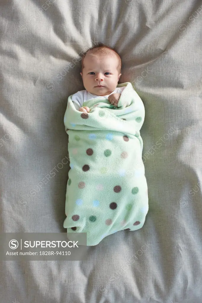 newborn baby girl in a white undershirt sleeping on a bed swadled in a baby blanket, Ontario, Canada
