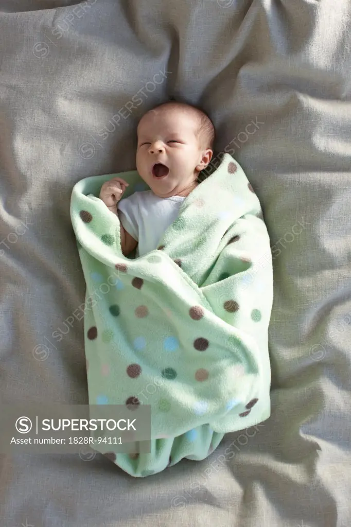 caucasian newborn baby girl in a white undershirt yawning on a bed swadled in a baby blanket