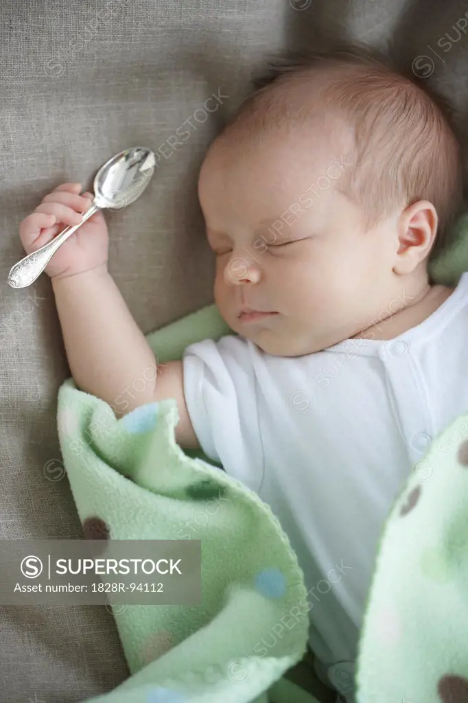 newborn baby girl in a white undershirt laying on a bed with a silver spoon in her hand, Ontario, Canada