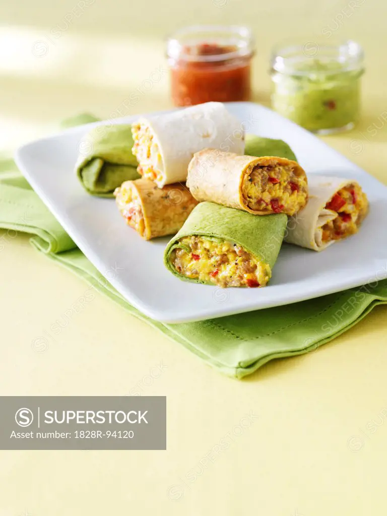 egg, meat and red pepper burrito breakfast wraps cut and stacked on a plate with salsa and guacamole