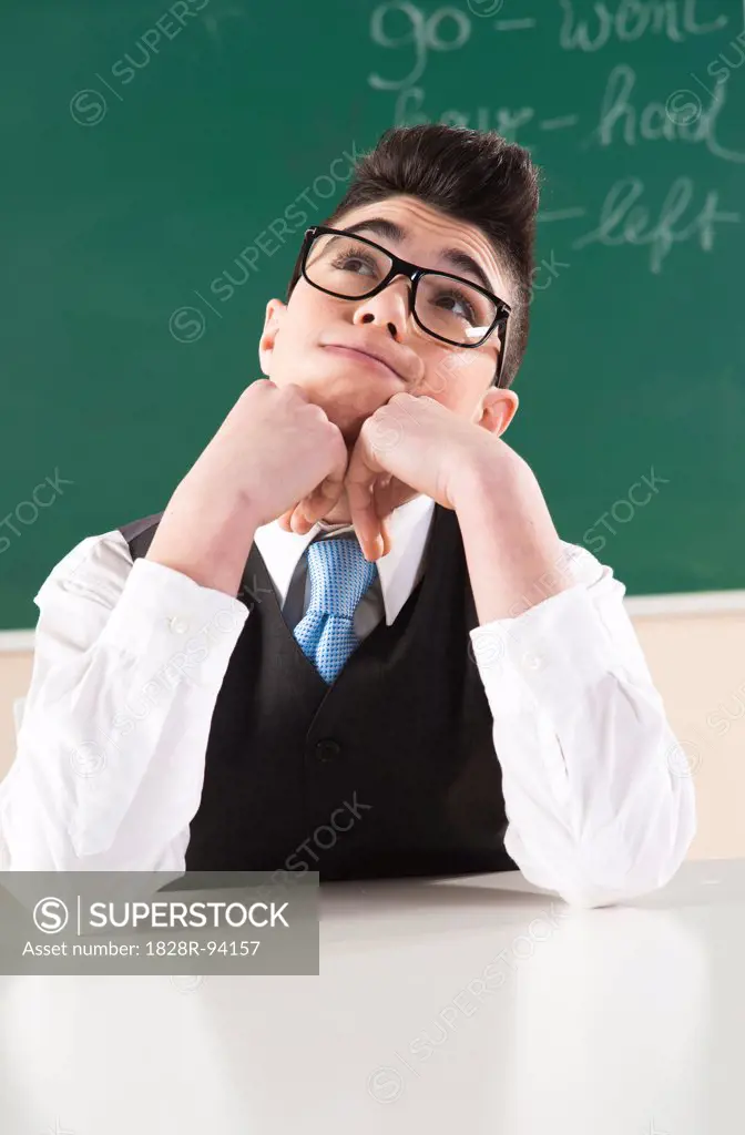 Boy Leaning on Hands in front of Chalkboard in Classroom