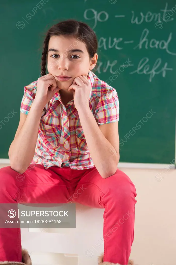 Portrait of Girl Sitting in Front of Chalkboard in Classroom