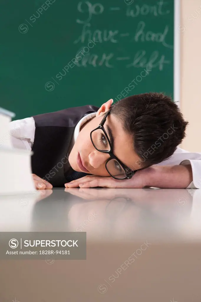 Boy with Head on Desk in front of Chalkboard in Classroom