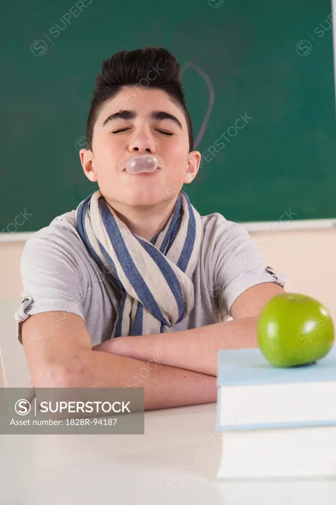 Boy with Eyes Closed and Blowing Gum Bubbles in Classroom