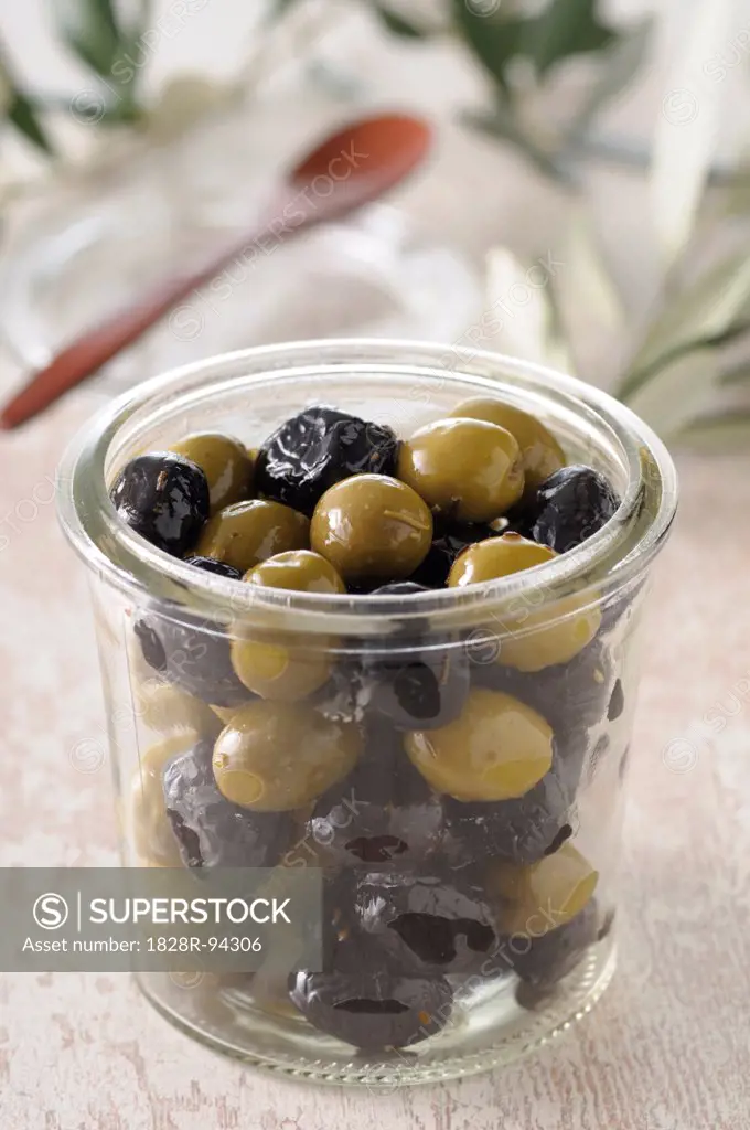 Close-up of Jar of Black and Green Olives with Wooden Spoon in Background