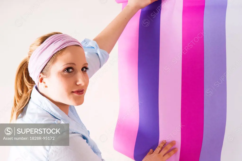 Studio Shot of Young Woman Holding Wallpaper up to Wall