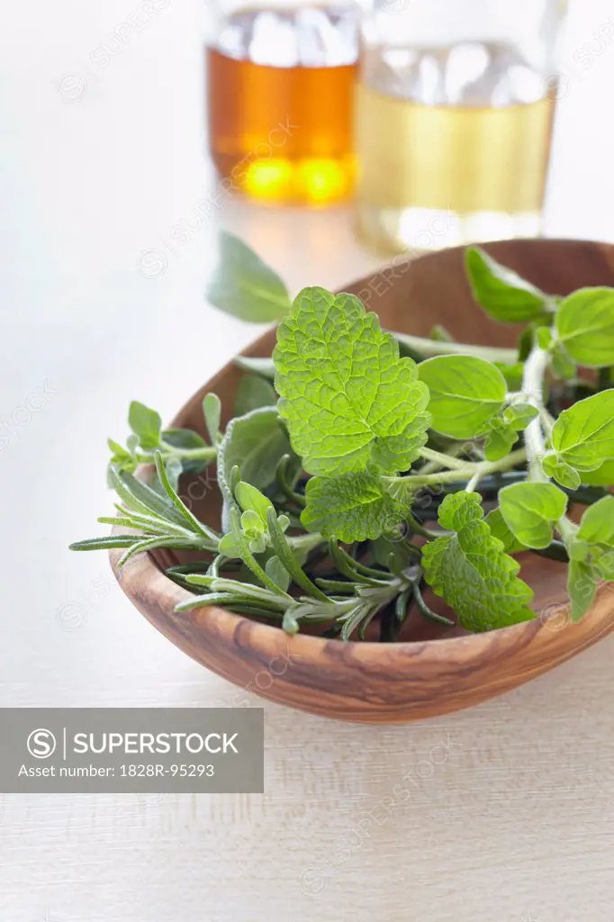 Fresh herbs in a bowl and bottles of oil for aromatherapy