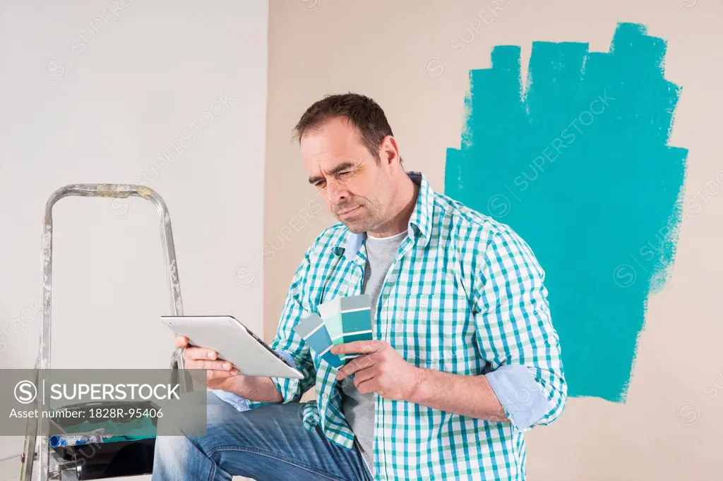 Mature Man Renovating his Home and Looking at Tablet Computer and Paint Samples
