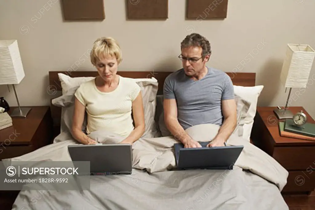 Couple with Laptops in Bed   