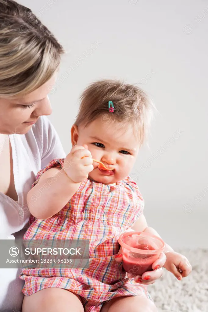 Portrait of Baby Girl feeding herself on Mother's Lap, Studio Shot,04/26/2013