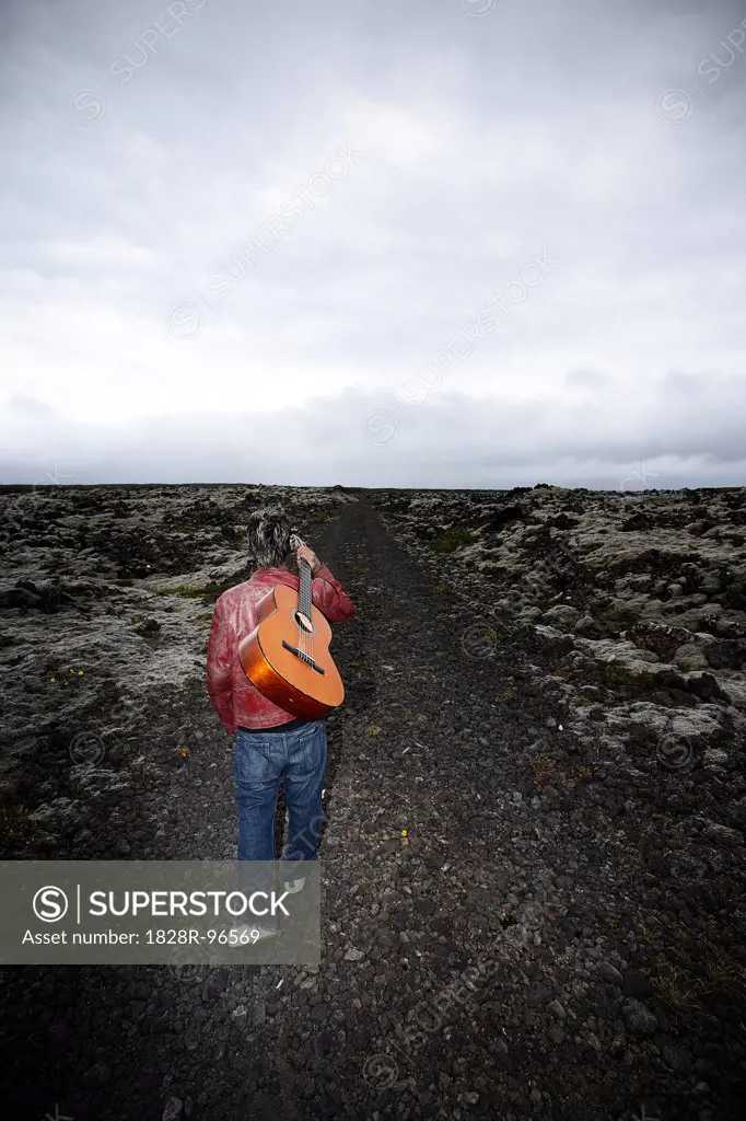 Young Man Carrying Guitar and Walking on Gravel Road, Iceland,08/25/2006