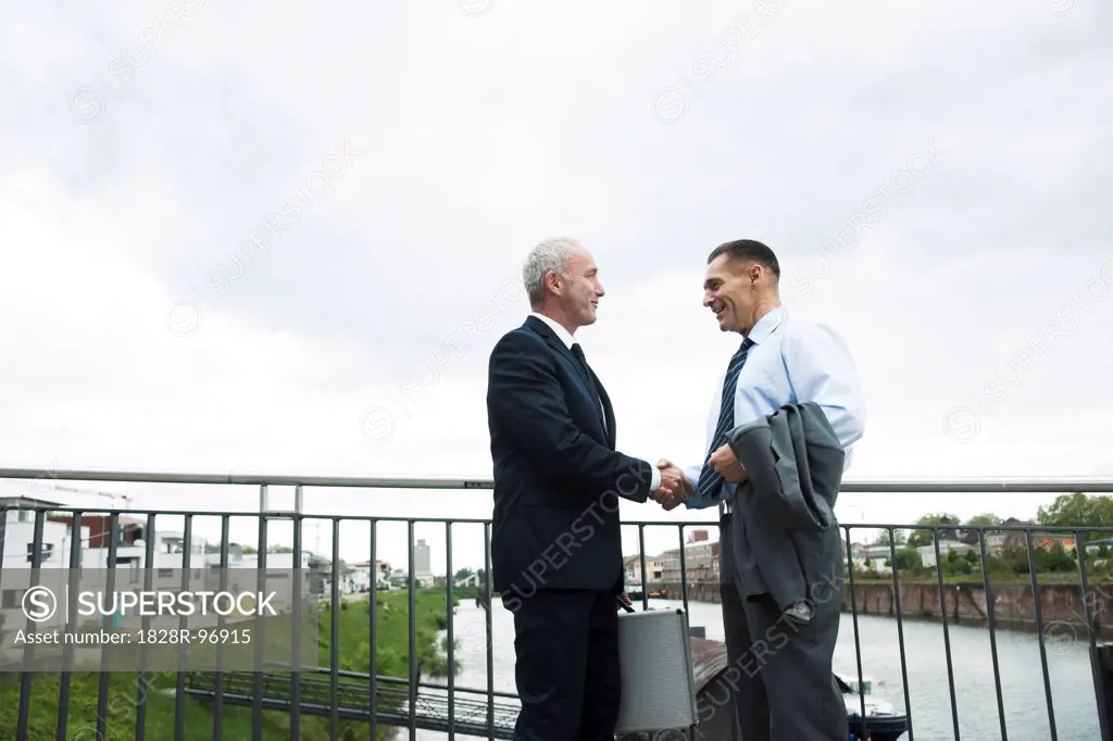 Mature businessmen standing by railing, shaking hands outdoors, Mannheim, Germany,05/11/2013