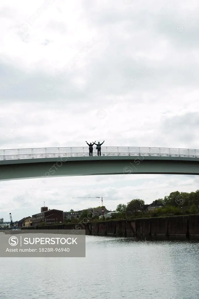 Silhouette of mature businessmen standing on bridge with arms in air, Mannheim, Germany,05/11/2013