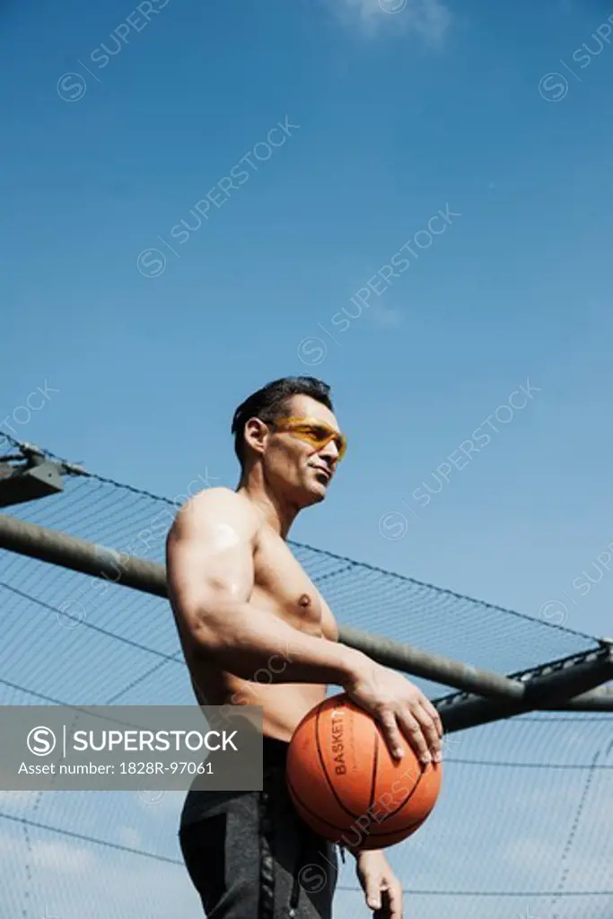 Mature man holding basketball, standing on outdoor basketball court, Germany,05/02/2013