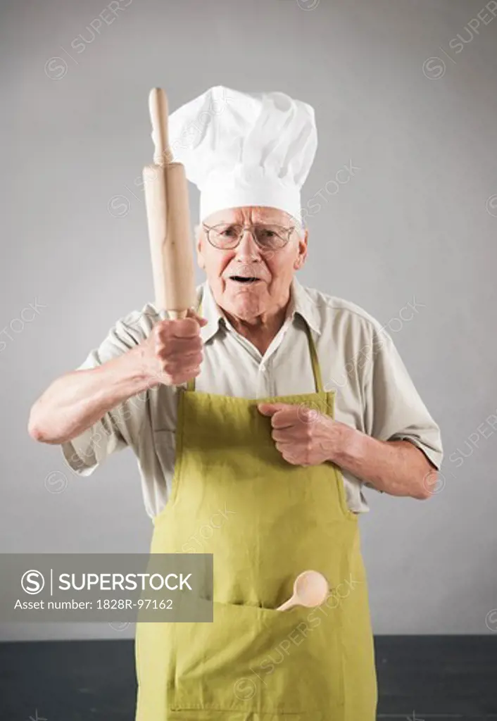 Elderly Man wearing Apron and Chef's Hat holding Rolling Pin in Studio,06/04/2013