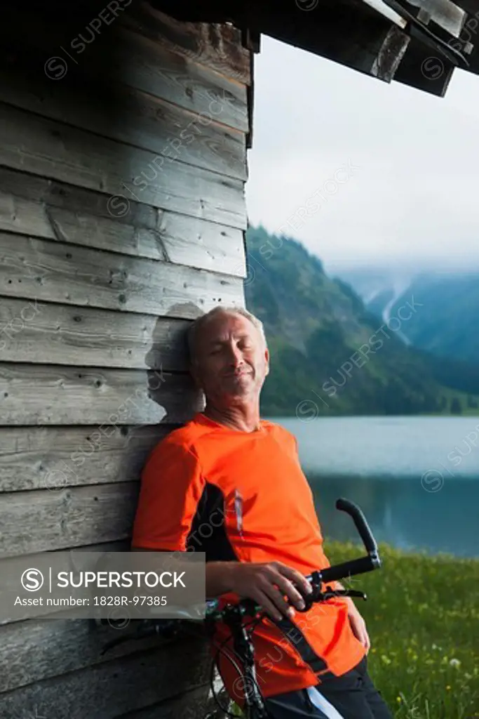 Mature Man leaning against Wooden Building with Mountain Bike, Vilsalpsee, Tannheim Valley, Tyrol, Austria,06/14/2013