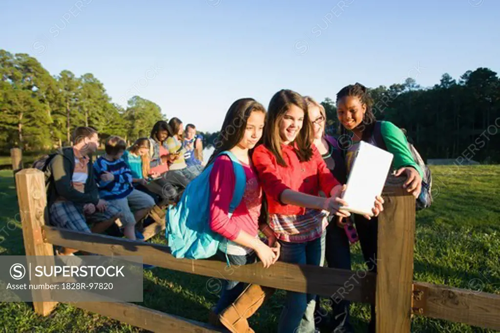 Group of pre-teens sitting on fence, looking at tablet computer and cellphones, outdoors,10/22/2012