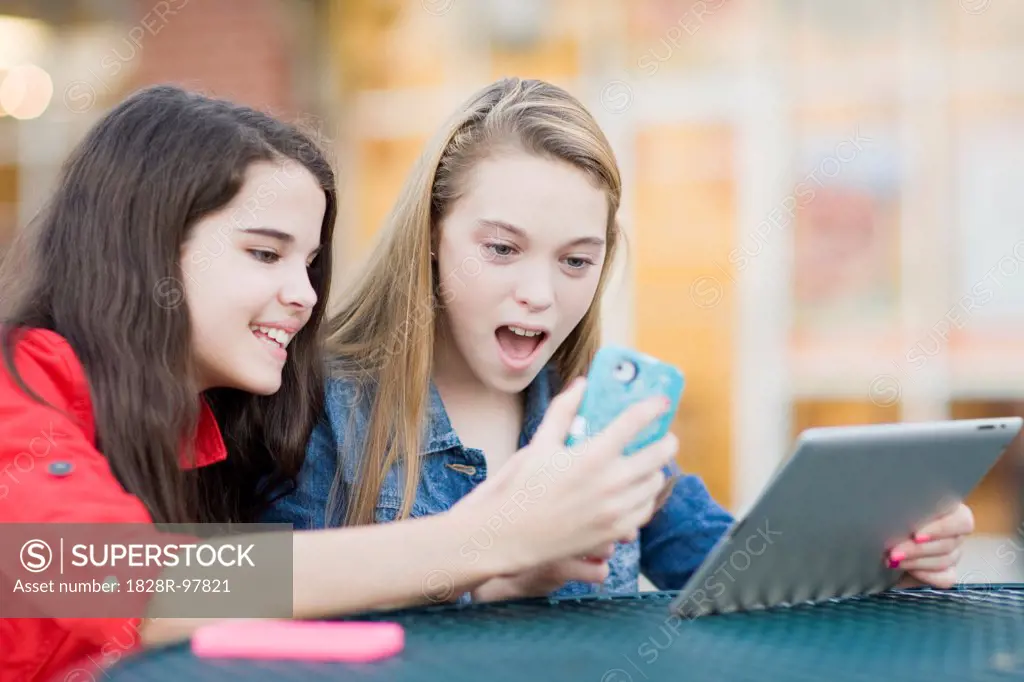 Pre-teen girls looking at cell phone and tablet computer, outdoors,10/11/2012
