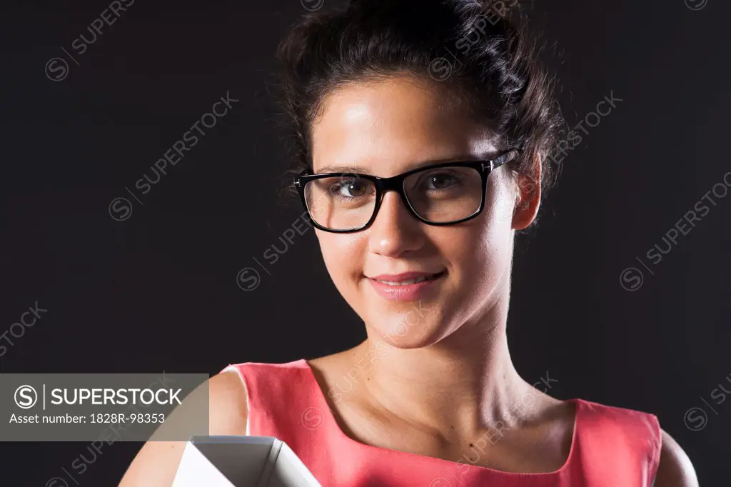 Close-up portrait of teenage girl wearing horn-rimmed eyeglasses, holding binder, smiling and looking at camera,07/12/2013