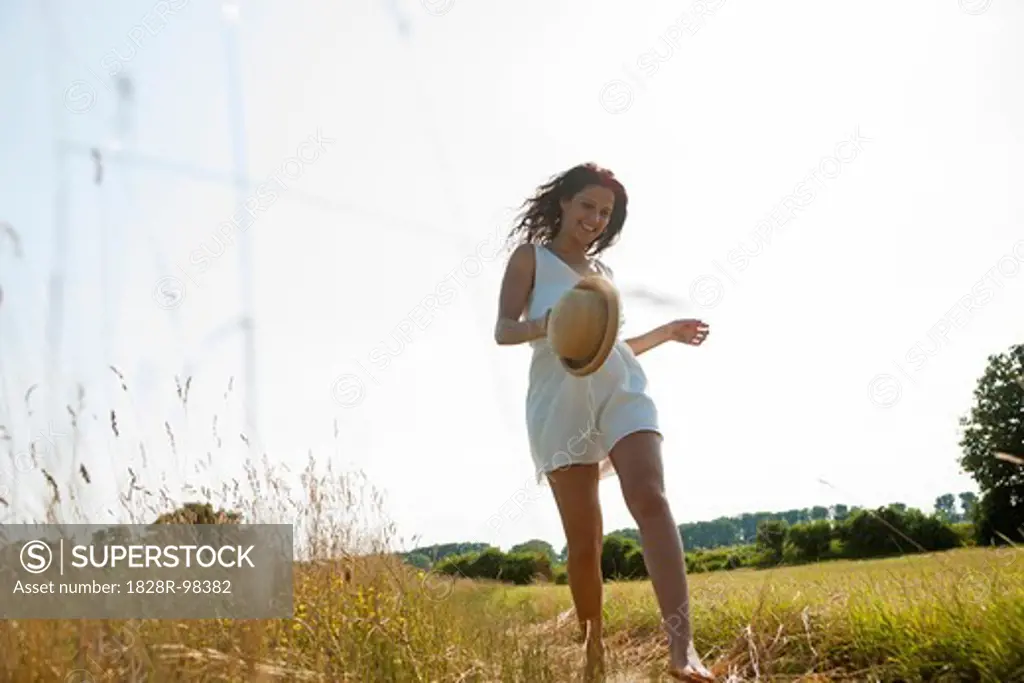 Teenaged girl holding straw hat and walking in field on summer day, Germany,07/12/2013