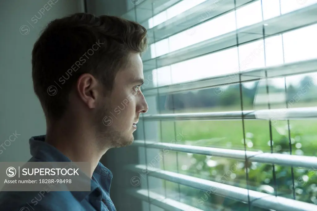 Close-up portrait of young man, looking out window through blinds, Germany,07/23/2013