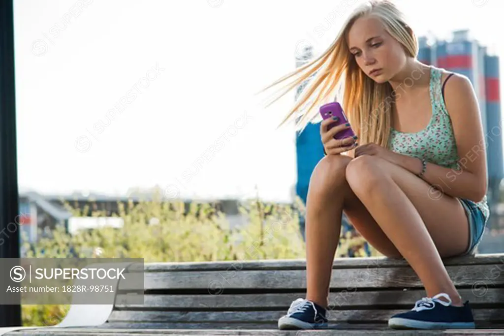 Teenage girl sitting on bench outdoors, looking at cell phone, Germany,08/21/2013